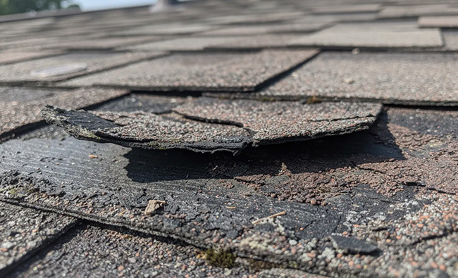 roof damage warning signs, missing and cracked asphalt shingles on a residential roof